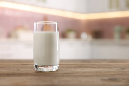 Glass of fresh milk on wooden table in kitchen. Space for text