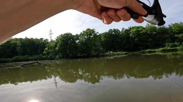 Cinematic POV of fisherman fighting a strong fish with bent rod against bright sun reflection on a serene forest lake.