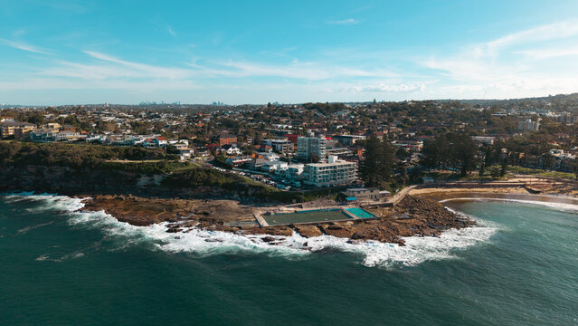 Aerial view of the Dee Why ocean pool on the rocky coastline with urban buildings and residential houses in the background under a clear blue sky Dee Why, New South Wales, Australia.