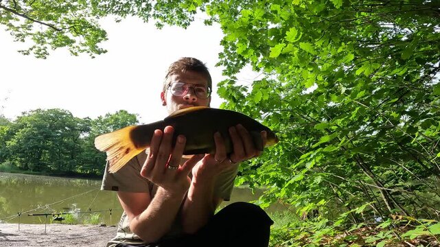 Young Fisherman Holding a Beautiful Caught Tench (Tinca tinca) by a Forest Lake on a Sunny Summer Day, Angling Success.