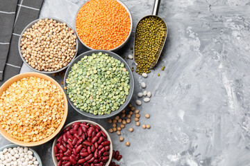 Fototapeta premium Different types of legumes in bowls on grey table, flat lay. Space for text