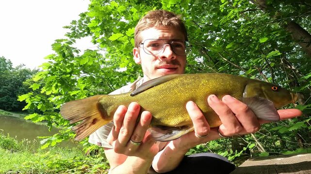 Young Fisherman Holding a Beautiful Caught Tench (Tinca tinca) by a Forest Lake on a Sunny Summer Day, Angling Success.