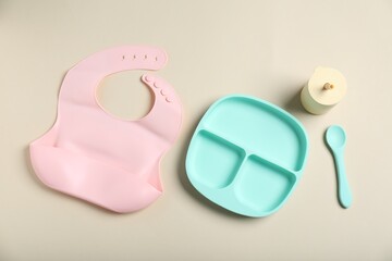 Obraz premium Set of baby tableware and silicone bib on beige background, flat lay