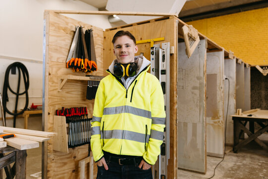 Smiling portrait of young male student with ear protectors around his neck at vocational workshop