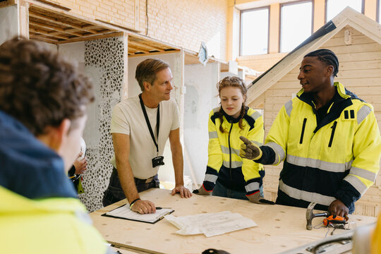 Young male student wearing reflective jacket discussing with instructor at civil engineering class in high school