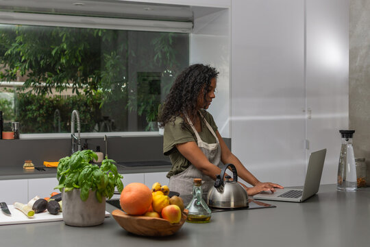 Side view of Hispanic woman using laptop in modern kitchen