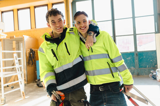 Smiling young male student wearing reflective jacket standing with arm around friend in vocational secondary school