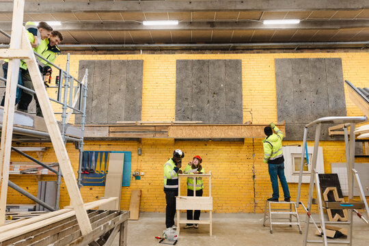 Vocational students doing various building tasks inside spacious construction workshop against yellow brick wall at scho