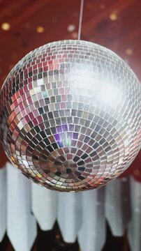 Vertical video. Close-up of mirror disco ball reflecting light at wedding party venue.