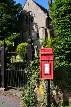A bright red postbox stands outside a church in rural Shropshire UK . Technology is overtaking the sending of paper letters with emails and texts replacing the letter.