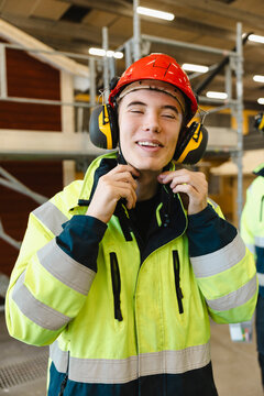 Smiling young male student wearing ear protectors and hardhat for construction work in workshop at vocational school