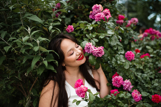 Beautiful adult woman 35-39 year old holding rose flowers with pink petals in garden close up. Natural beauty.