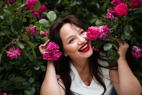 Beautiful adult woman 35-39 year old holding rose flowers with pink petals in garden close up. Natural beauty.