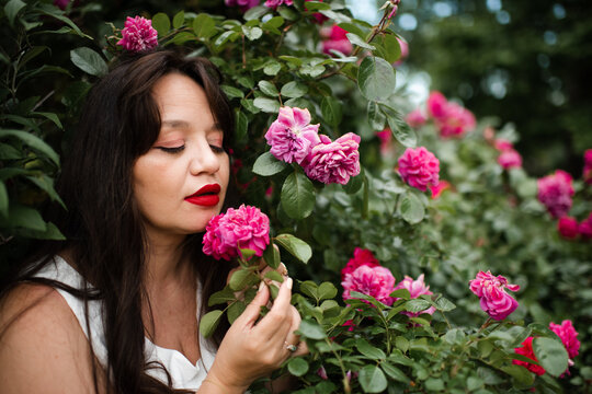 Beautiful adult woman 35-39 year old holding rose flowers with pink petals in garden close up. Natural beauty.