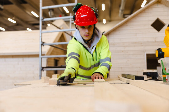 Focused young male student measuring wooden plank with ruler while training in construction work at vocational secondary