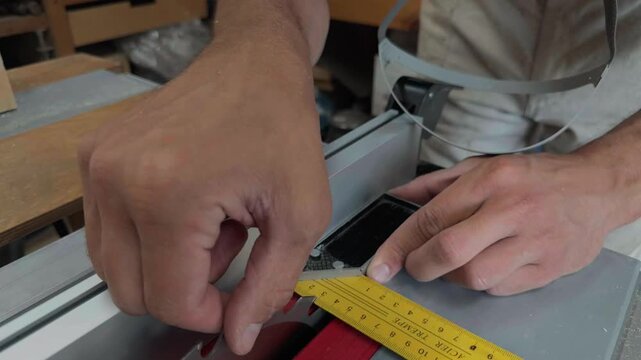 Extreme close up of unrecognizable artisan hands using a yellow square gauge to calibrate the sharp blade angle of a heavy table saw inside a joinery studio focusing on precise machinery setup