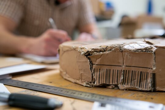 Damaged shipping carton with ruler and logistics supervisor recording package damage