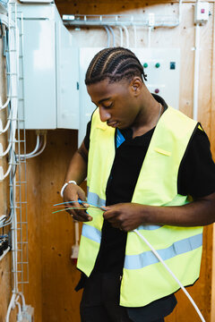 Concentrated young male trainee wearing reflective vest stripping insulation coating from colorful electrical wires usin
