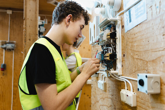 Young male student inserting electrical wiring into open terminal block components mounted on wooden mockup board in wor