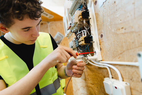 Male student tightening components with screwdriver on wall mounted electrical breaker panel in training workshop