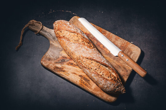 Freshly baked rustic bread baguette with seeds on wooden cutting board with knife