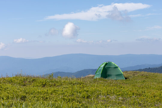 a green dome tent pitched on a grassy mountain ridge under a blue sky with copy space.