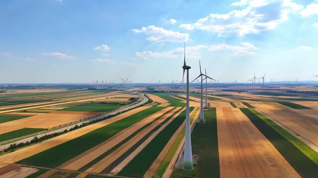 Wind turbines and rural road, aerial farmland. Turbine in foreground, distant turbines and paved road, patchwork fields below