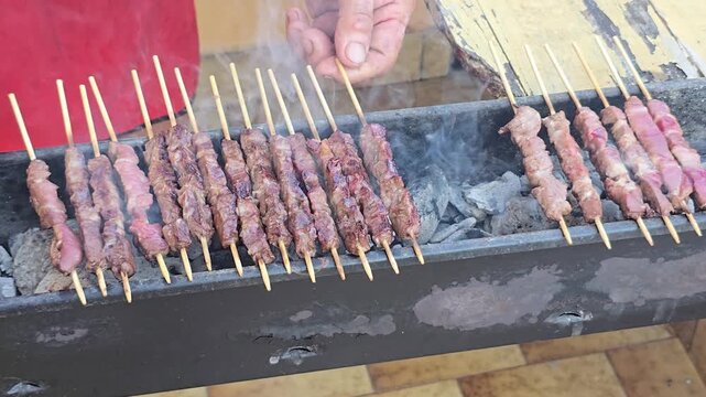 Traditional Italian arrosticini lamb skewers grilling on narrow charcoal barbecue canalina preparing delicious regional meat street food delicacy during outdoor party in Italy concept.