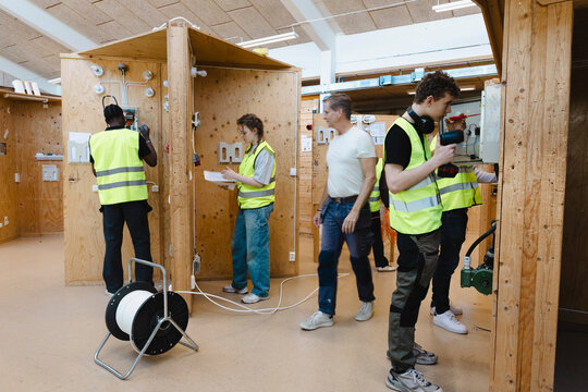 Male professor observing young students repairing electrical outlets at wooden stand in training center