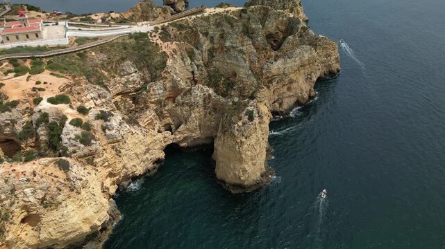 Wide drone panorama of Ponta da Piedade coastline, featuring cliffs, boats, sea stacks, walking paths and the full Atlantic landscape of Lagos, Portugal.