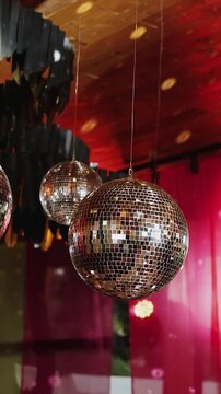Vertical video. Reflective mirror disco balls hanging above wedding celebration with warm lighting.