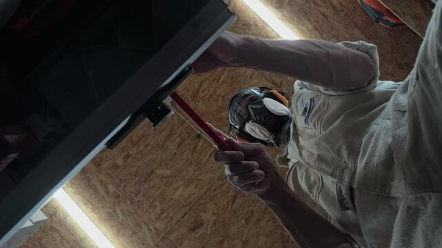 Anonymous male woodworker in full protective gear safely ripping a timber block on a table saw with a red push stick inside a cluttered workshop overhead top down ceiling handheld perspective