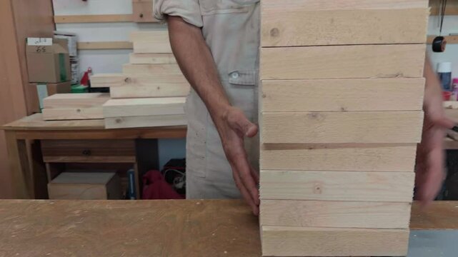 Authentic male fabricator organizing a neat stack of identical pine blocks on a workroom bench dynamic handheld tracking shot with a ninety degree camera roll following the material arrangement