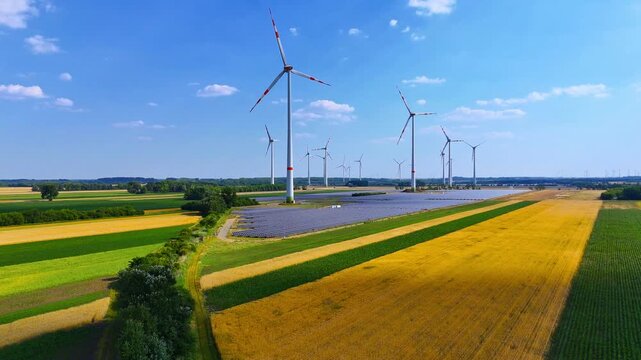 Wind turbines and solar panels above wheat field. Row of turbines with solar array, golden field, aerial drone perspective, clear