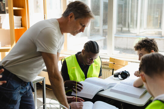 Male teacher assisting students studying vocational subject in classroom at high school