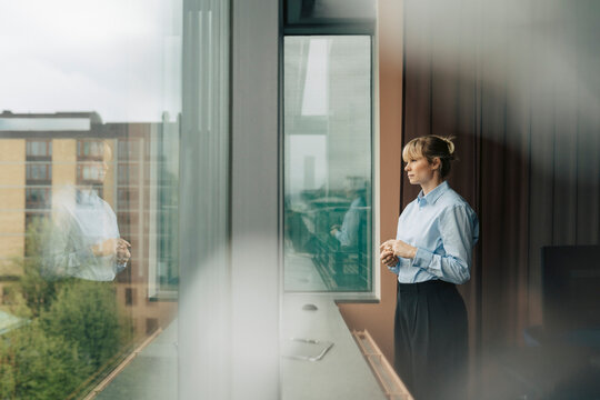 Thoughtful female business expert looking out through window glass while standing near sill in office