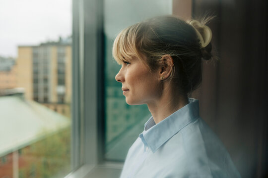 Side view of businesswoman with bangs looking out through window at office