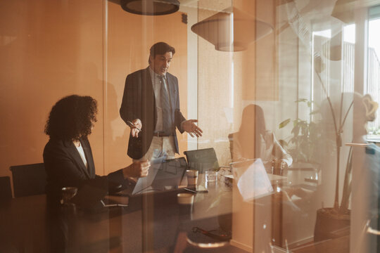 Male business expert pitching sales ideas to team in glass-walled conference room at office