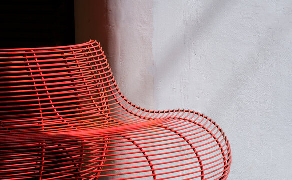 Modern red metal wire bench against white concrete wall, minimalist urban street furniture design with shadow.