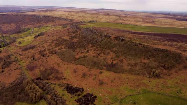 Drone footage of autumnal view at Baslow Edge and Curbar Edge in Peak District UK, lower altitude hills with rocky edges seen from a high point of view.