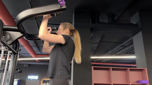 Athletic woman performs an assisted pull-up on a strength machine, training her back and upper body in a modern gym