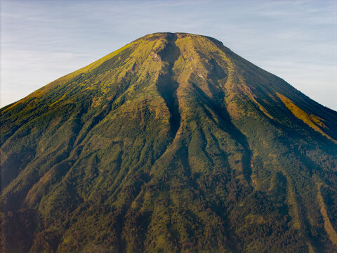 Aerial view of the lush green slopes of Mount Tambi with deep volcanic ravines and dense vegetation under clear morning light, Kejajar, Central Java, Indonesia.