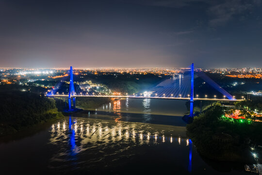 Aerial view of the illuminated Integration Bridge spanning the river at night, with city lights glowing in the background in Foz do Iguacu, State of Parana, Brazil.