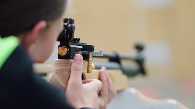Young person aiming at target with air rifle during practice session at shooting range