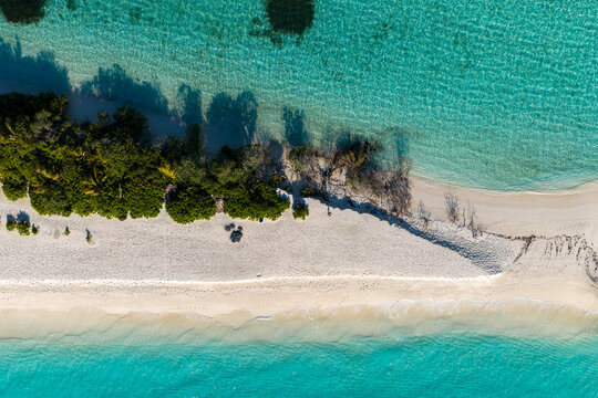 Aerial top down view of Dhigurah Island, Maldives, with a slender sandbar, white sand beach, coral shallows, deeper lagoon, rippling water, and midday light.