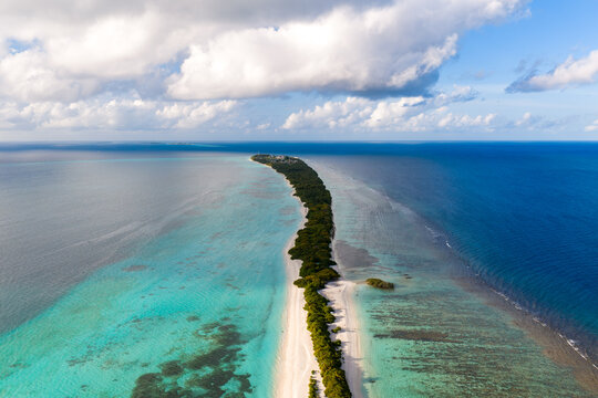 Aerial view of Dhigurah Island, Maldives, long sandbar with patchy coral reefs, gentle waves along the reef edge, soft tropical daylight, elongated form to horizon.