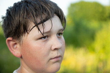 sad boy with wet hair and tears looking away in outdoor greenery setting close-up side profile portrait children's emotions brown green natural light clean background copy space editorial. © Liudmila