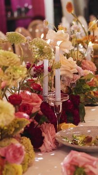 Vertical video. Wedding banquet table with floral arrangements and burning candles outdoors.