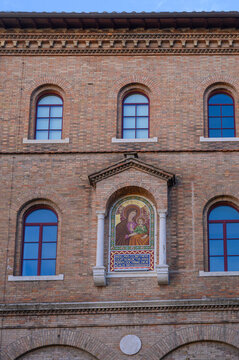 Detailed view of the brick wall fa&ccedil;ade of Sant'Anselmo Church in Rome, featuring arched windows and a central architectural niche with a golden mosaic depicting the Madonna and Child