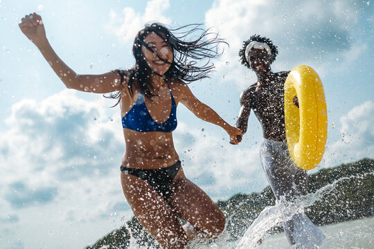Friends, diverse couple having fun with colorful inflatable rings at the seaside